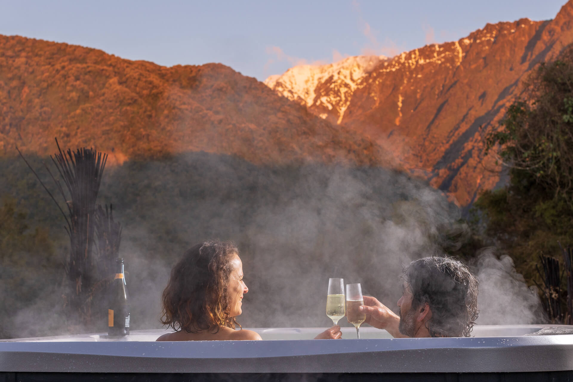 Guests enjoying a wine in the spa looking at the snowy mountain range behind them