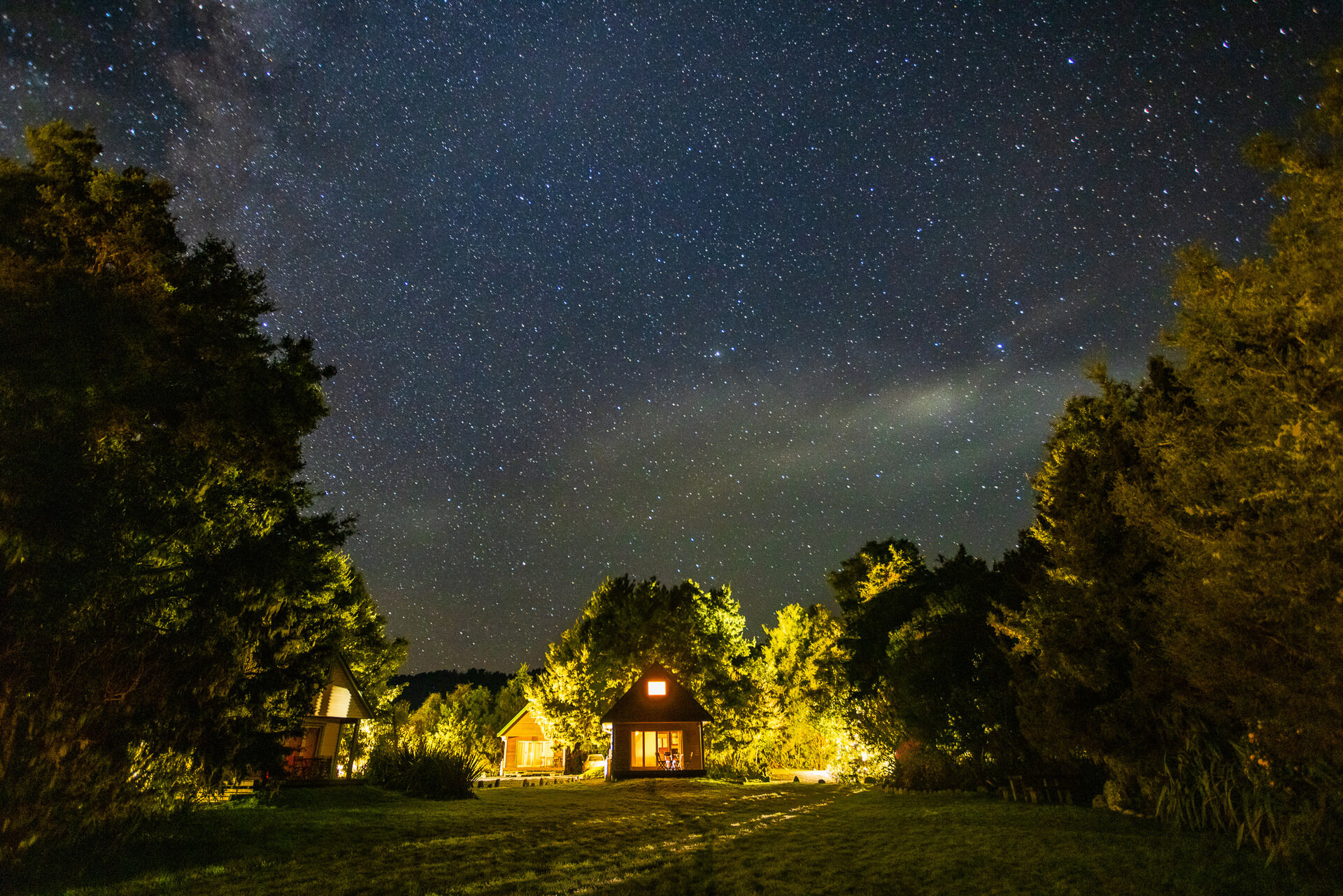 Chalets with lights on surrounded by trees and starry skies above
